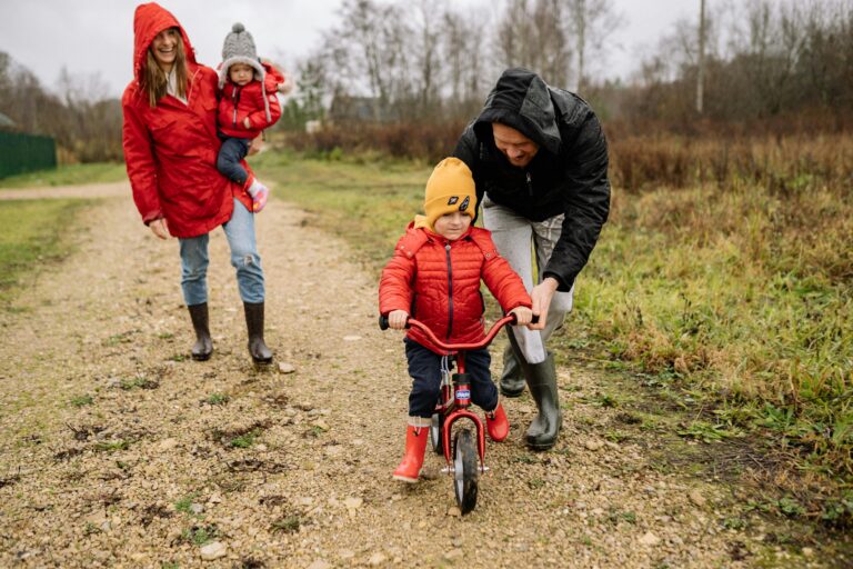 Happy family walking outdoors in fall, teaching child to ride bike.